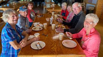Group of people sitting at a table eating pancake breakfast and smiling