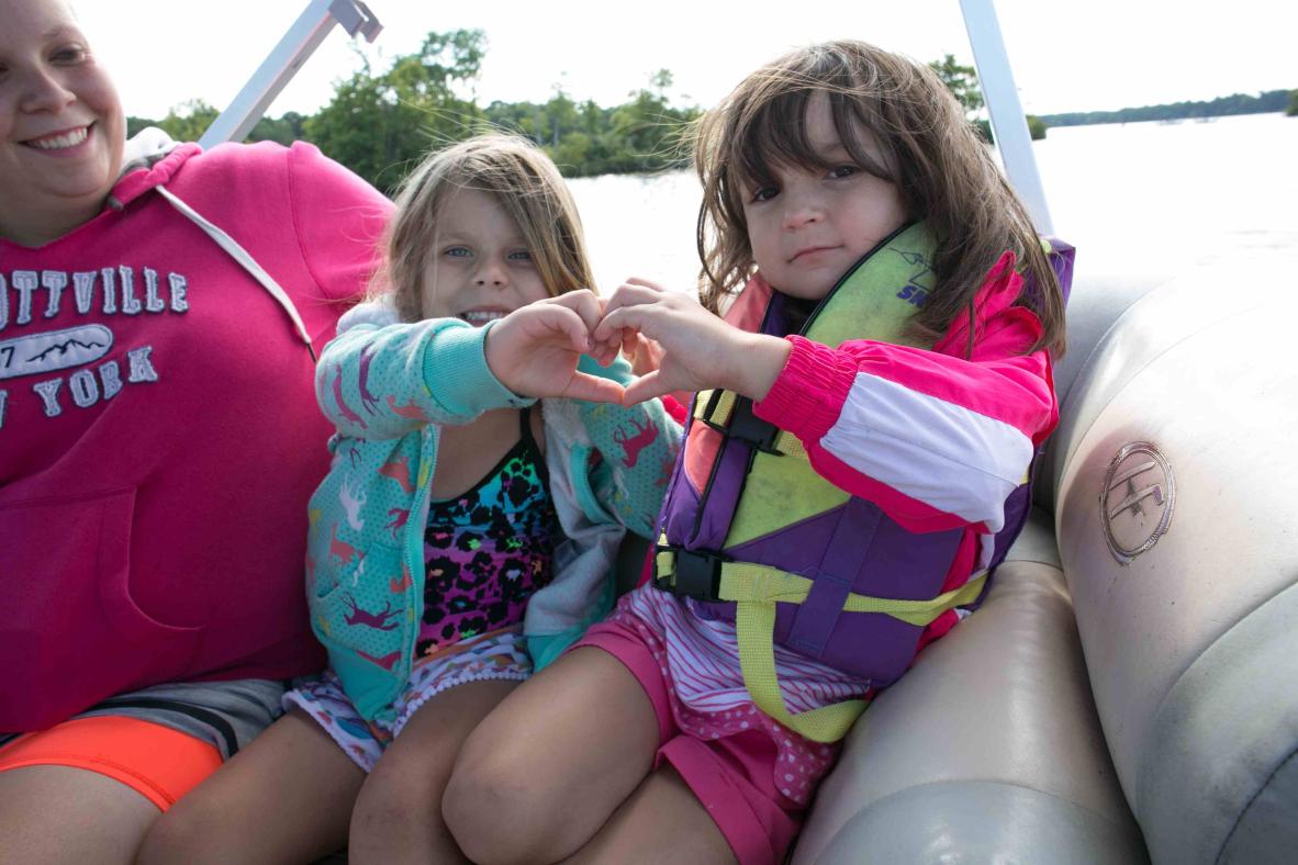 Friends making a heart with their hands on a boat.