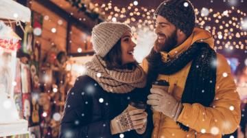 Smiling couple in holiday scene outside holding warm beverages 