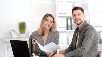 Young adult woman showing young adult man a brochure.  Both are smiling at the camera.