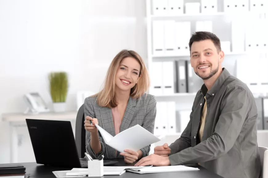 Young adult woman showing young adult man a brochure.  Both are smiling at the camera.